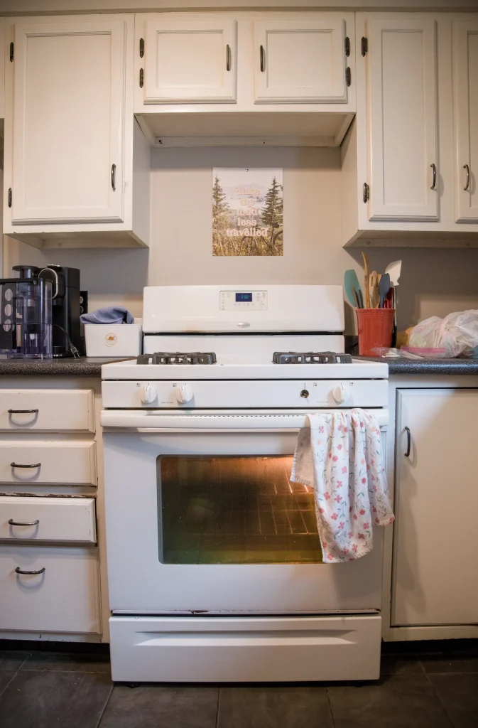 An entry-level white gas stove with the oven light on, positioned centrally in a white kitchen.